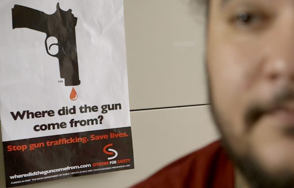 Kevin Thomas posing in front of gun buy back poster - C300 screen grab