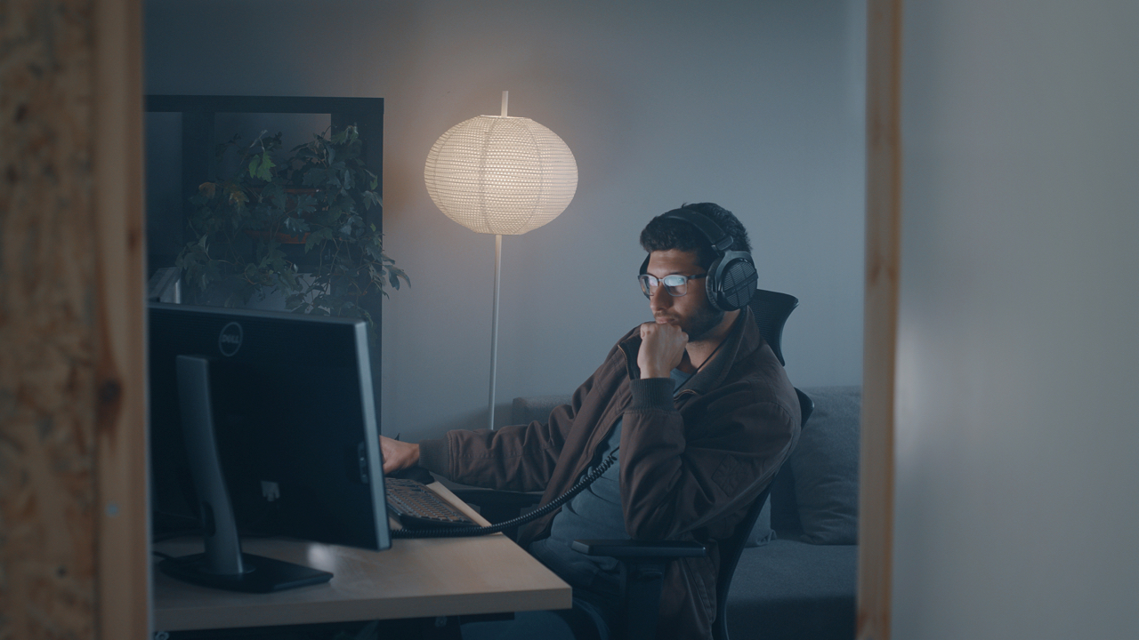 A man looks at his computer, listening to music from Artlist while wearing headphones 